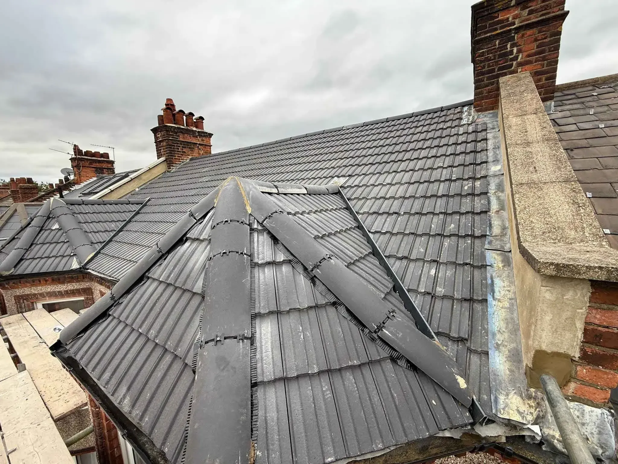 Completed charcoal-grey tiled roof with dry ridge tiles and a chimney stack in Hither Green, Greater London
