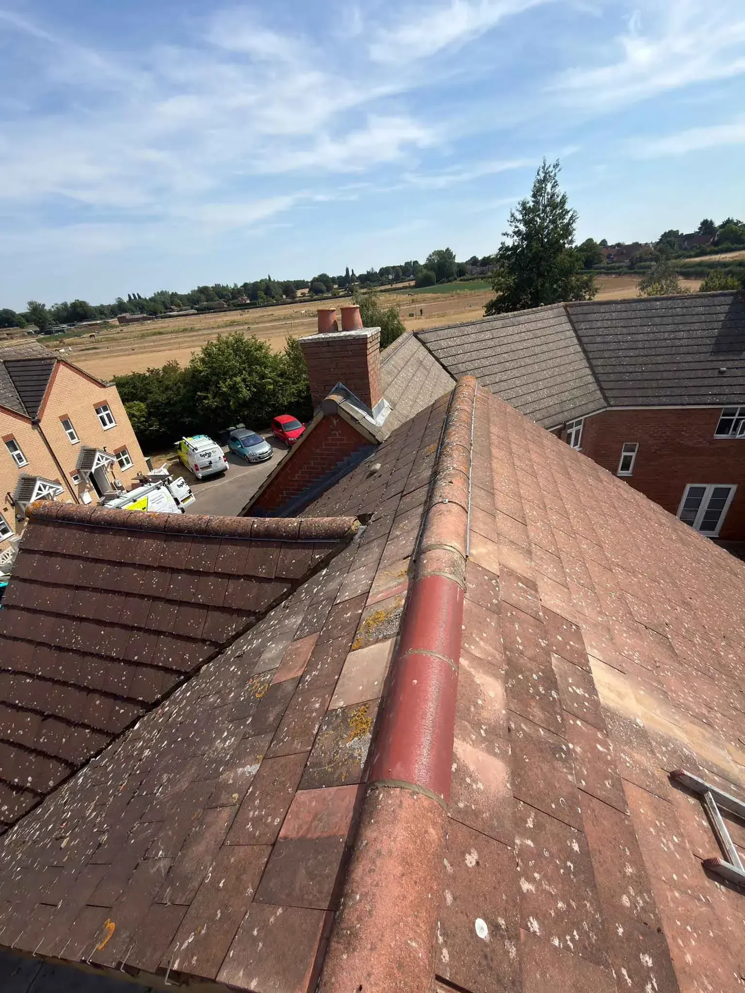 Re-bedded ridge tiles on a tiled roof in Ascot, Berkshire, with neighbouring houses and fields beyond