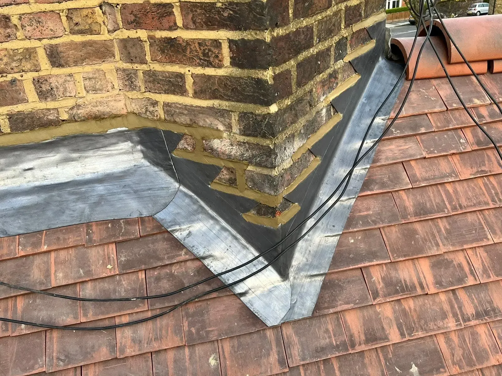 Lead flashing overview at a chimney-to-roof junction on a tiled roof
