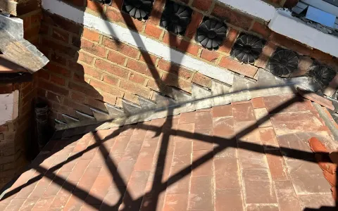 Lead step flashing at a pitched porch roof and brick wall junction in West Drayton