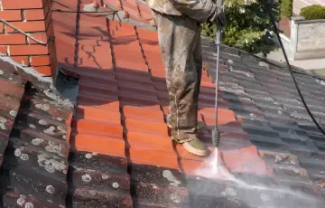 A roofer pressure-washing moss from a tiled roof